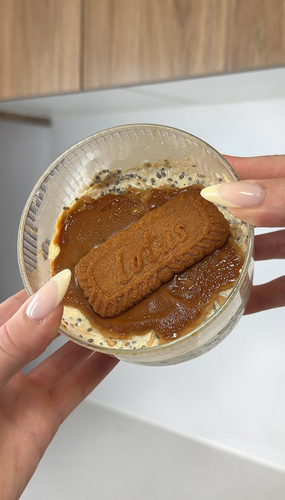 Hand holding a tub of Biscoff protein overnight oats topped with caramel sauce and a Lotus Biscoff biscuit
