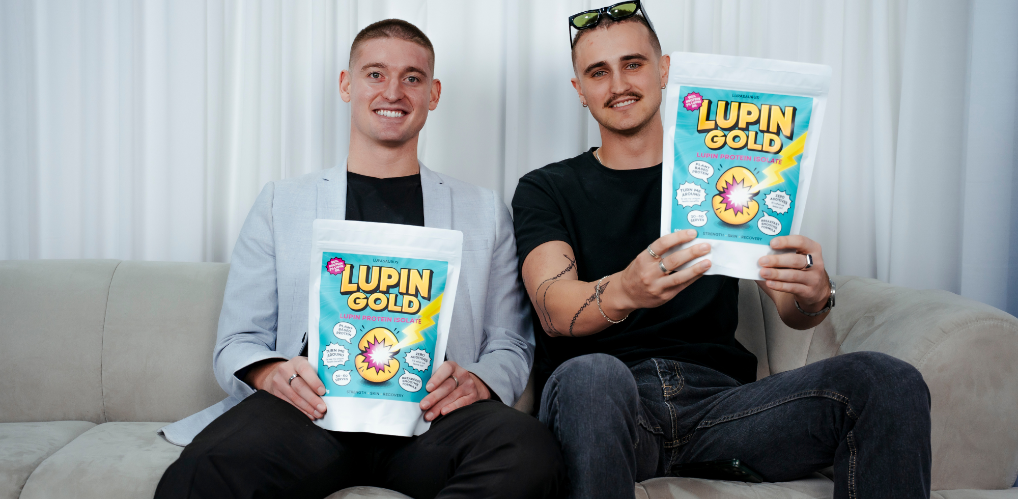 Kobi and Harvie sitting on a couch holding Lupin Gold plant protein products.