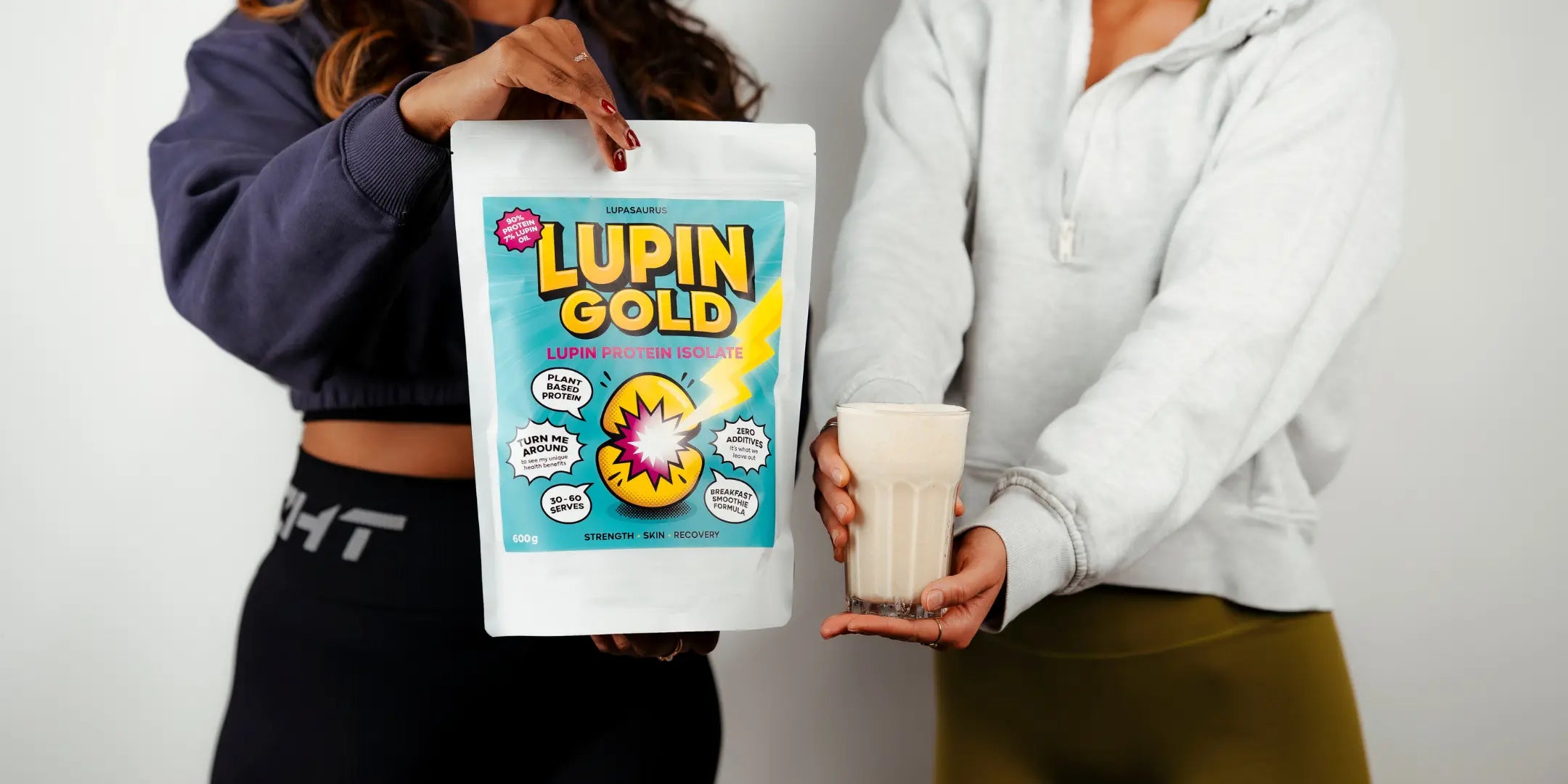 Two people holding a bag of Lupin Gold protein powder and a glass of a Lupin protein and banana smoothie.