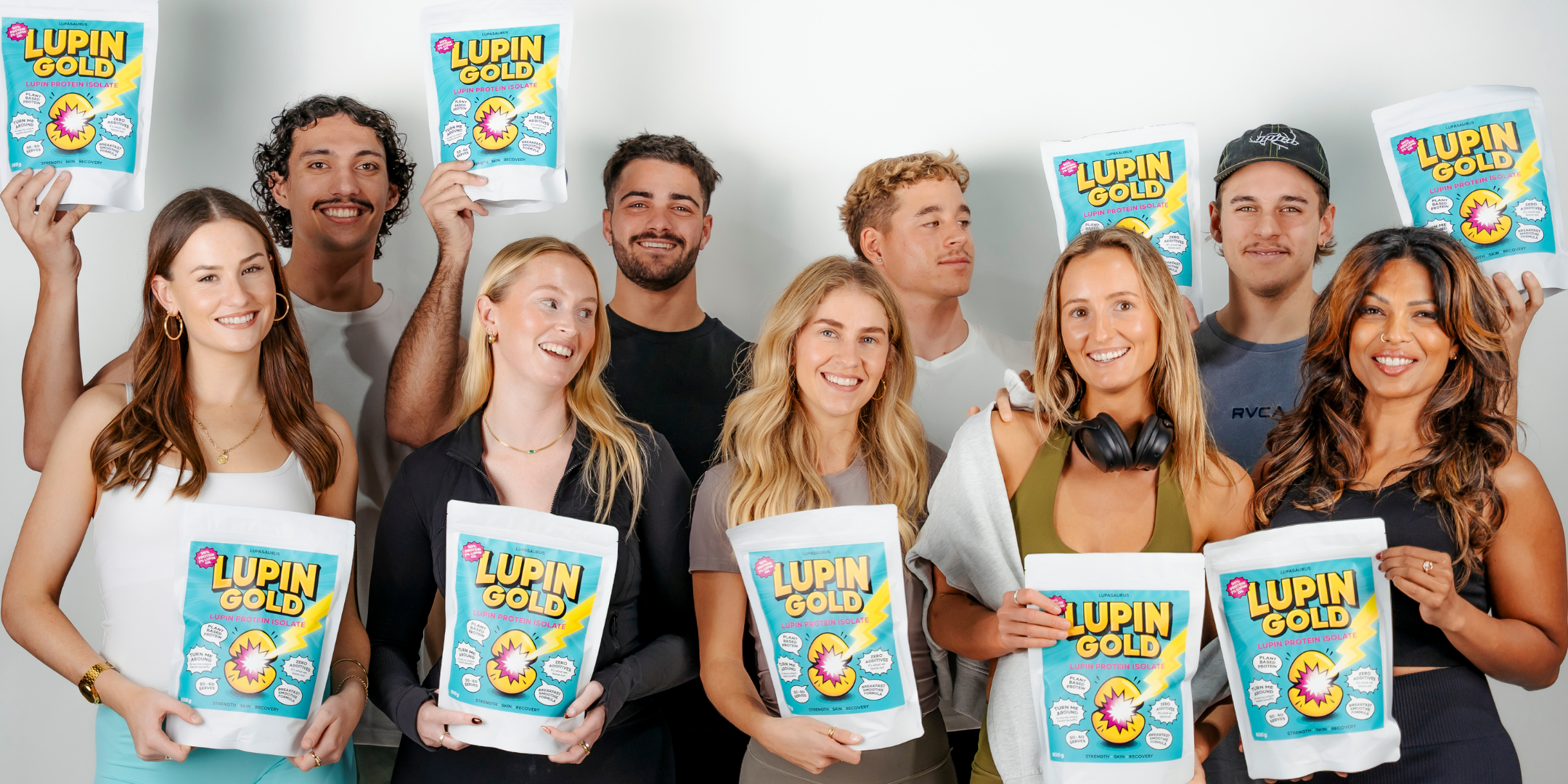 Group of people holding Lupin Gold protein isolate powder packets against a plain background