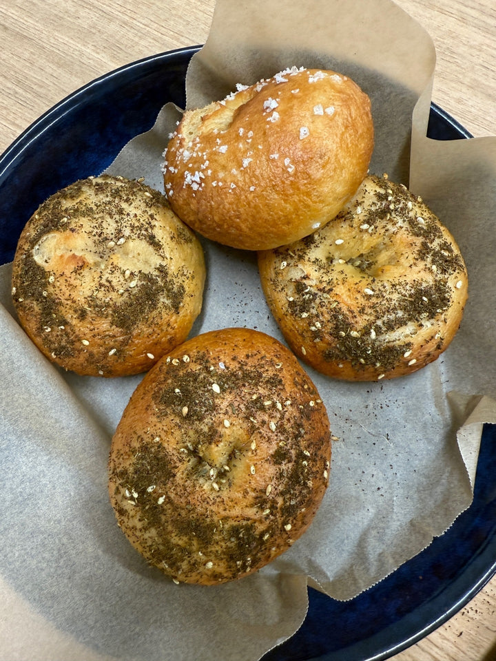 Four seeded lupin flour bagels in a blue bowl lined with baking paper, three topped with everything seasoning and one with salt