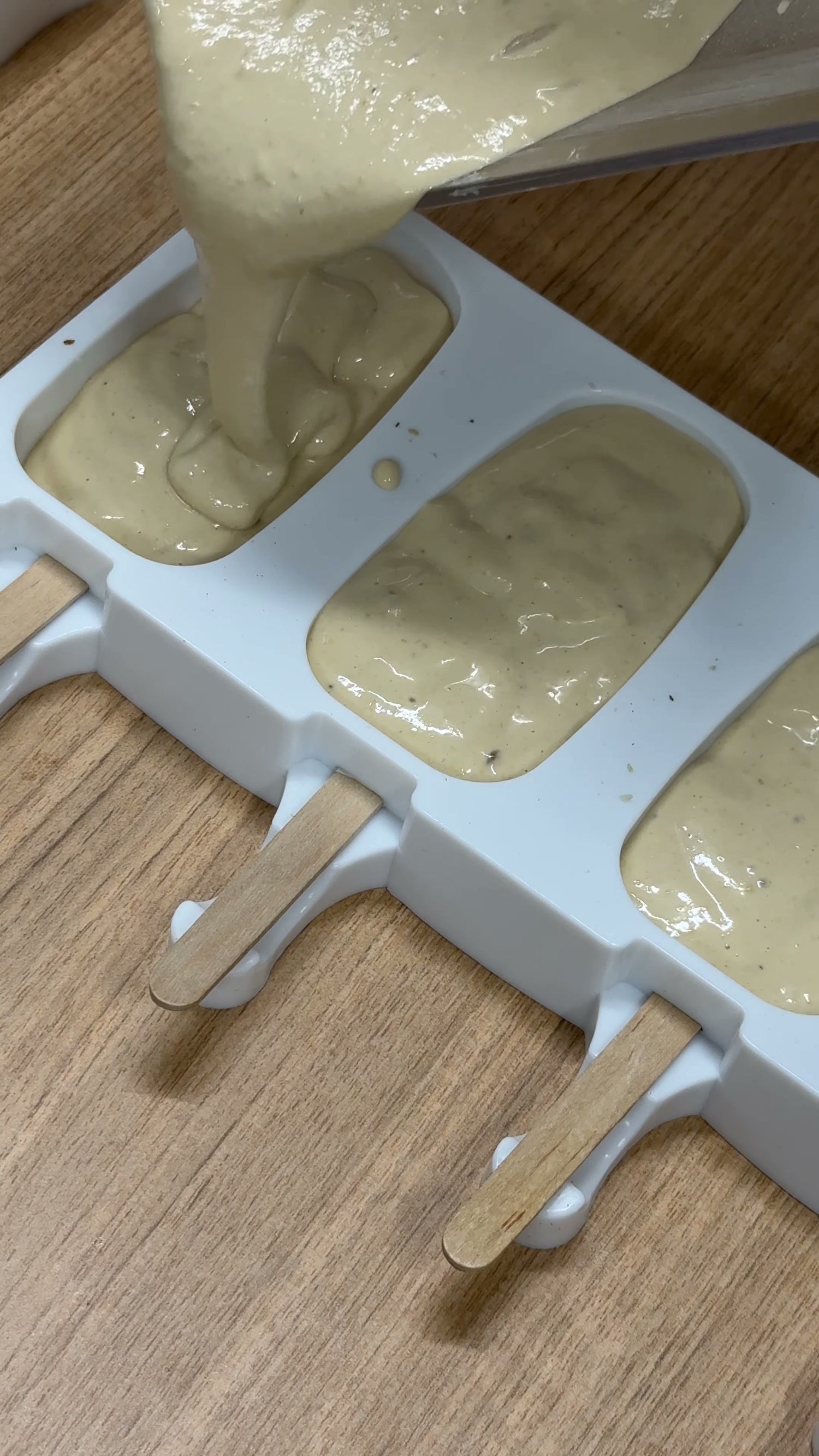 Ice cream bar mixture being poured into a silicone mould with wooden sticks in place