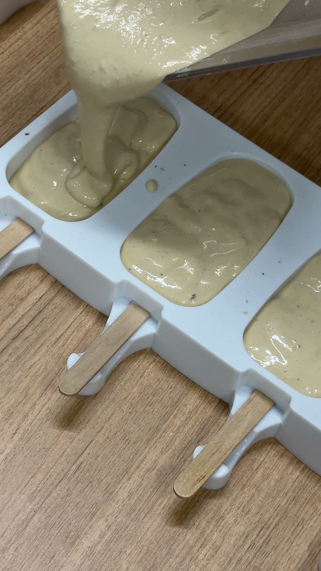 Ice cream bar mixture being poured into a silicone mould with wooden sticks in place