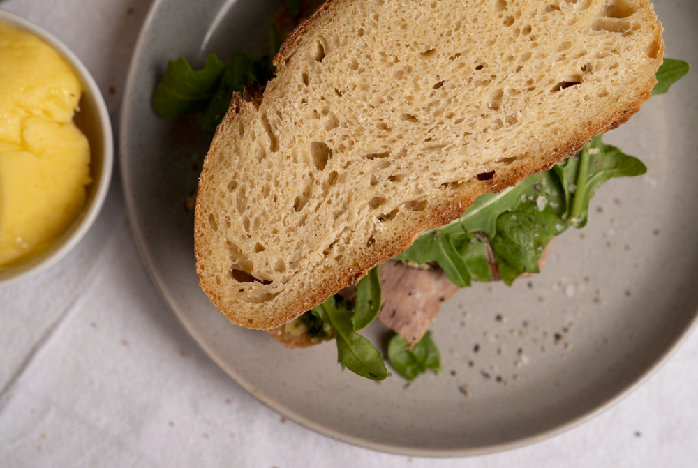 Thick-cut sourdough sandwich filled with rocket on a grey plate beside a dish of butter