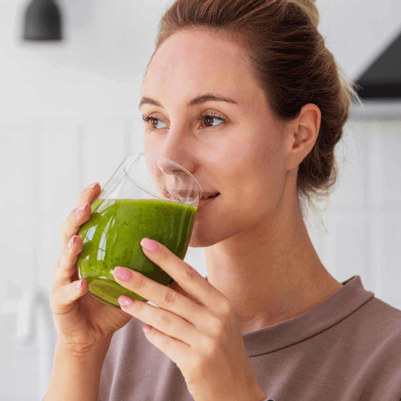 Woman drinking a green lupin protein isolate smoothie in a kitchen setting