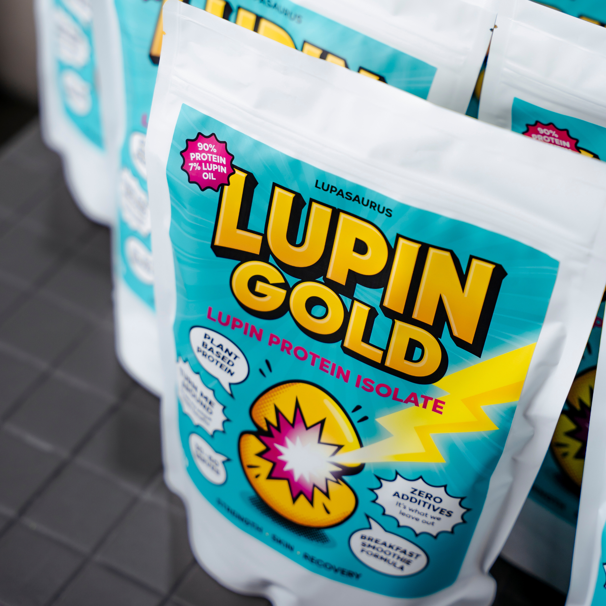 Packets of Lupin Gold lupin protein isolate with colorful packaging on a tiled surface.