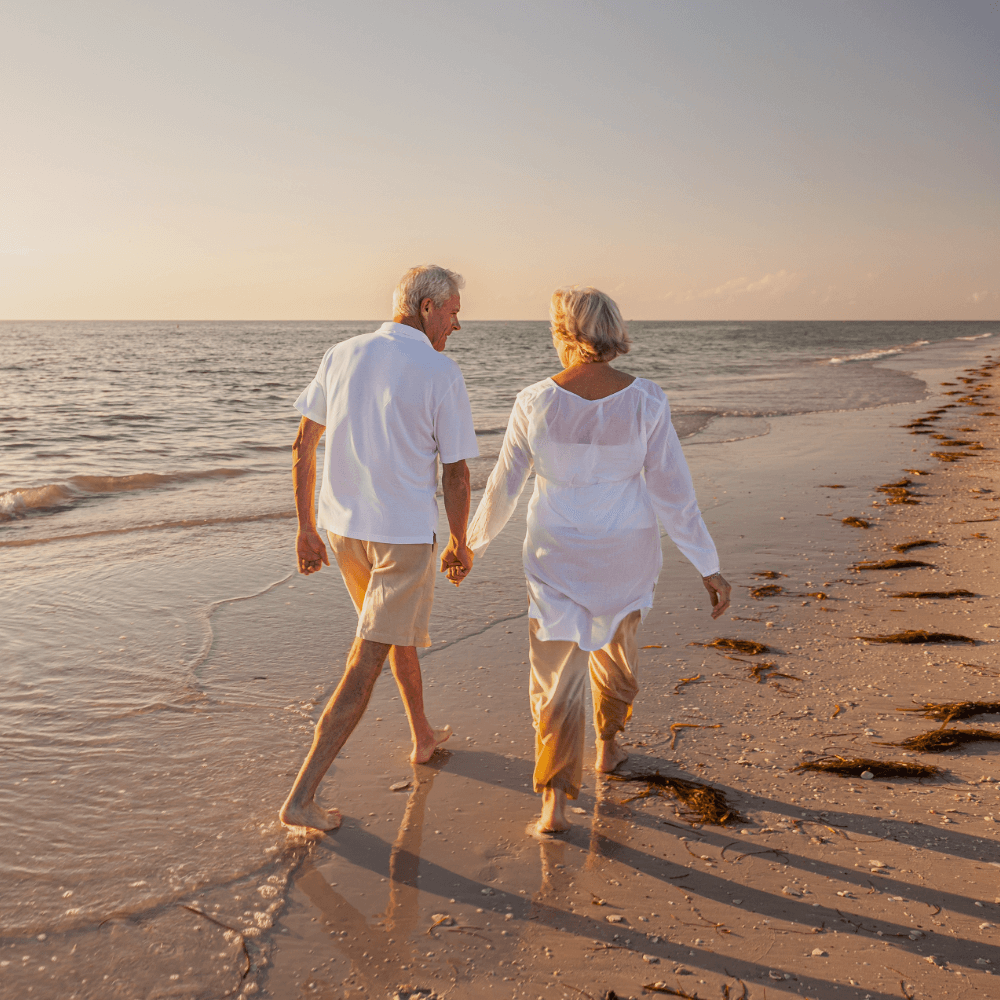 Senior couple walking hand in hand on a beach at sunset.