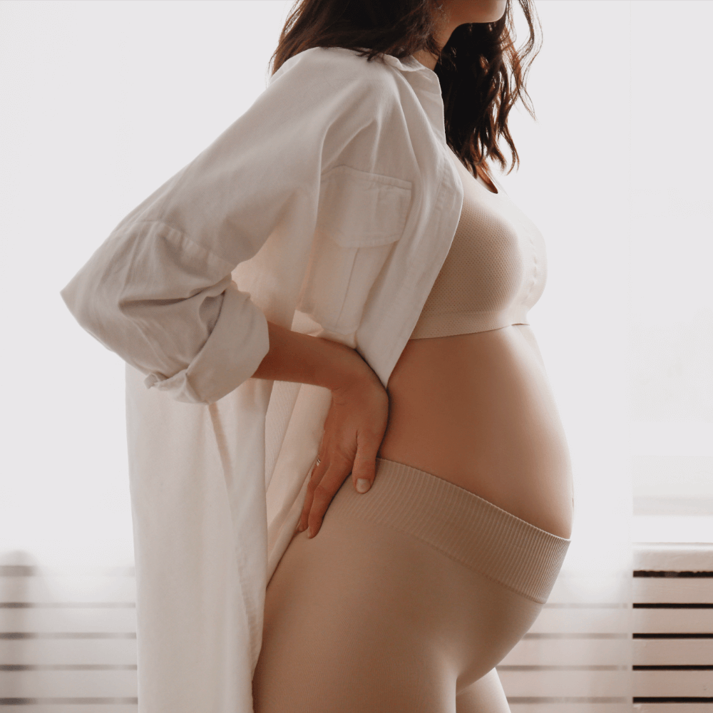 Pregnant woman wearing a white shirt and beige leggings indoors.